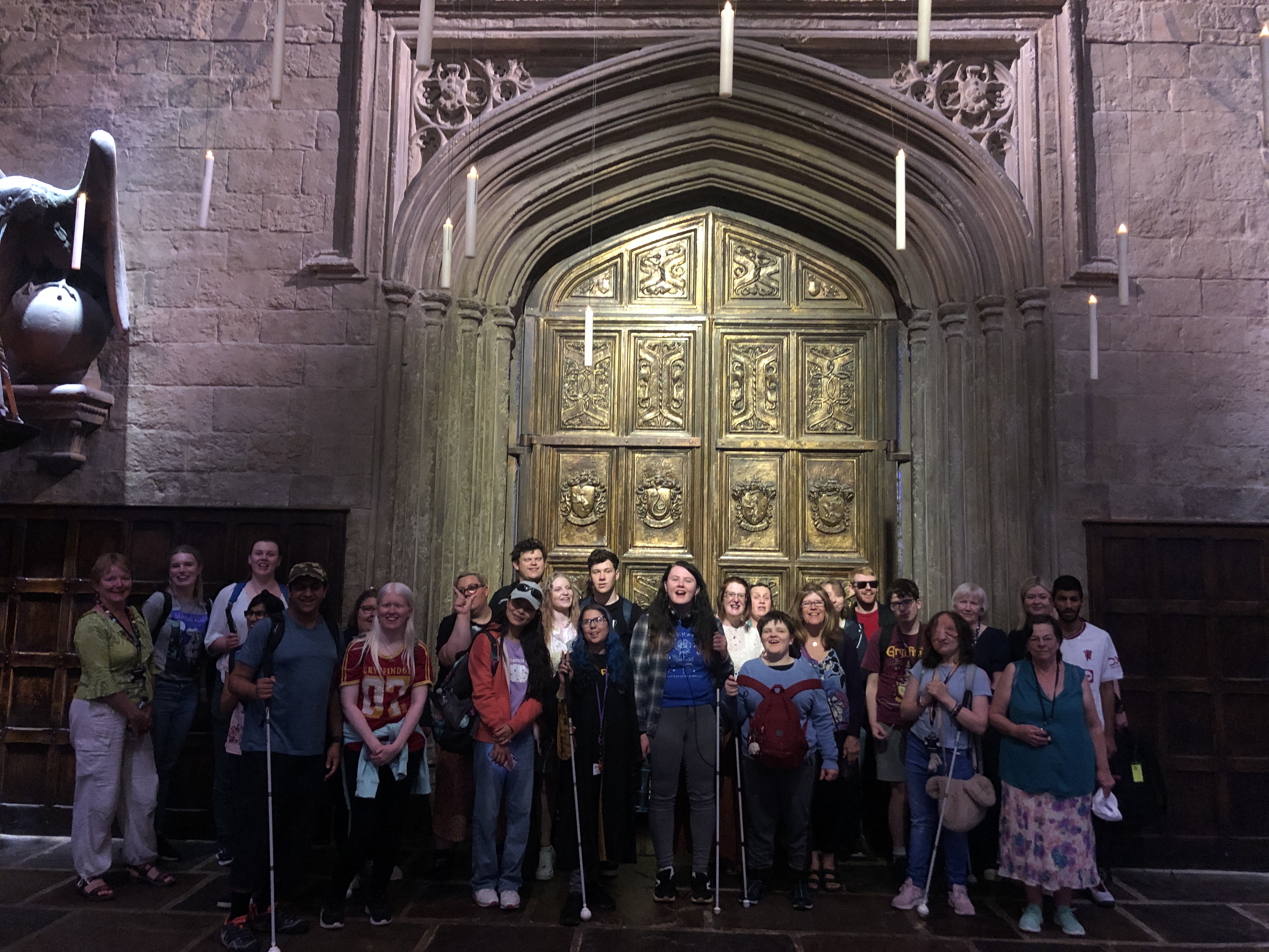 the group of staff and students stand in front of the giant entrance to the great hall