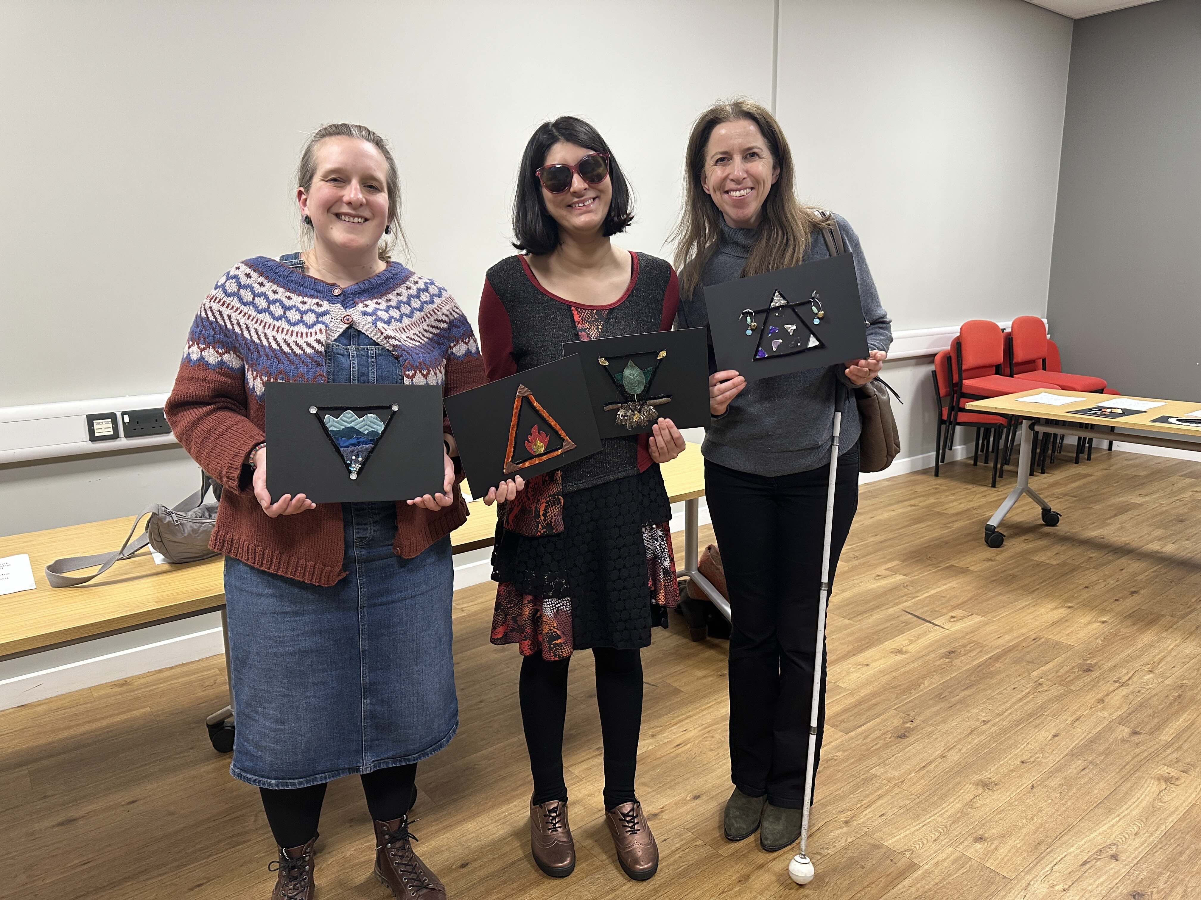 two representatives from Look UK stand with Maleeka - they all hold up tactile art pieces from the exhibition