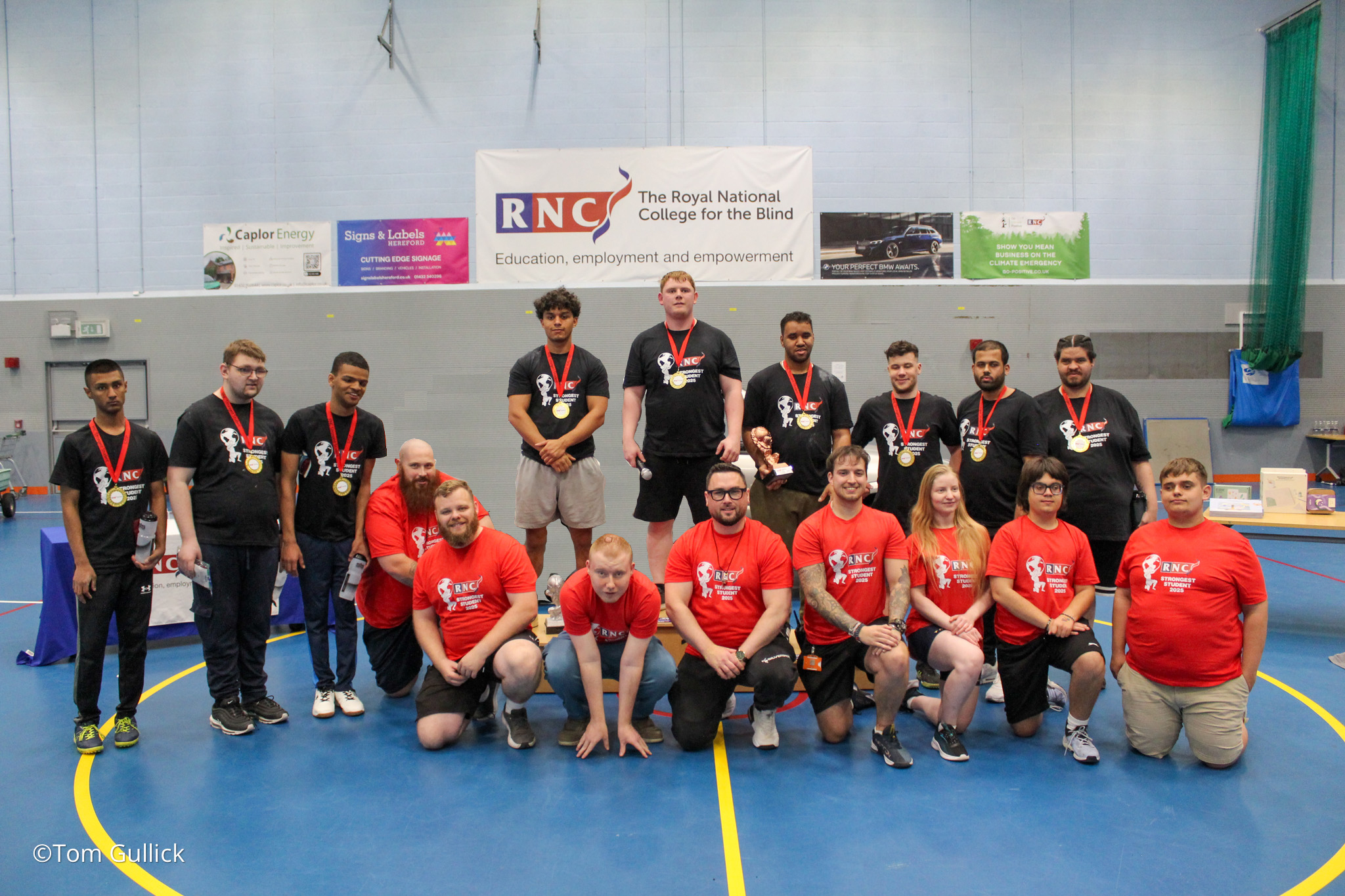 The group of competitors, judges and volunteers stand and kneel in a group