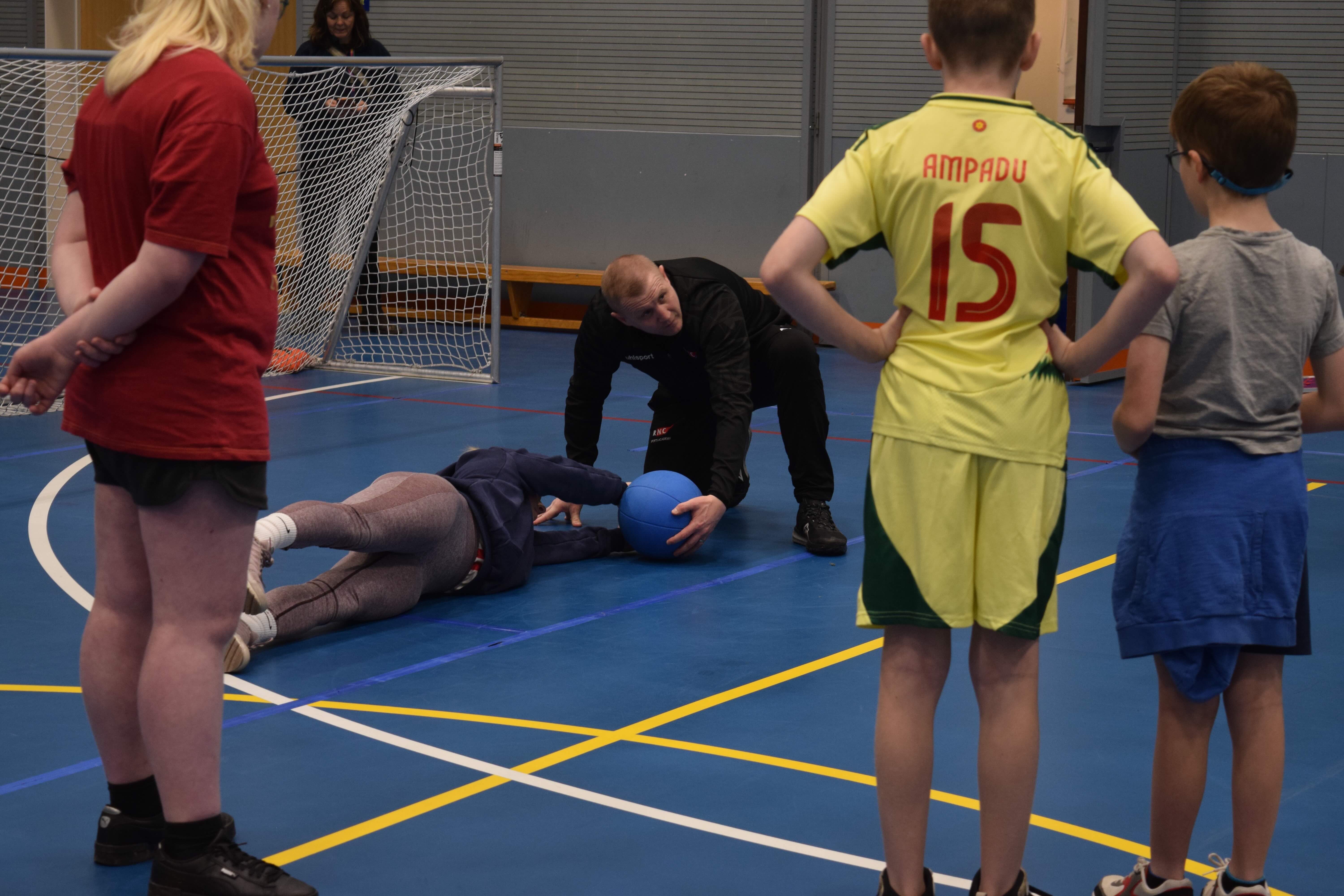 a goalball instructor with a player demonstrating how to defend a ball as 3 young people look on