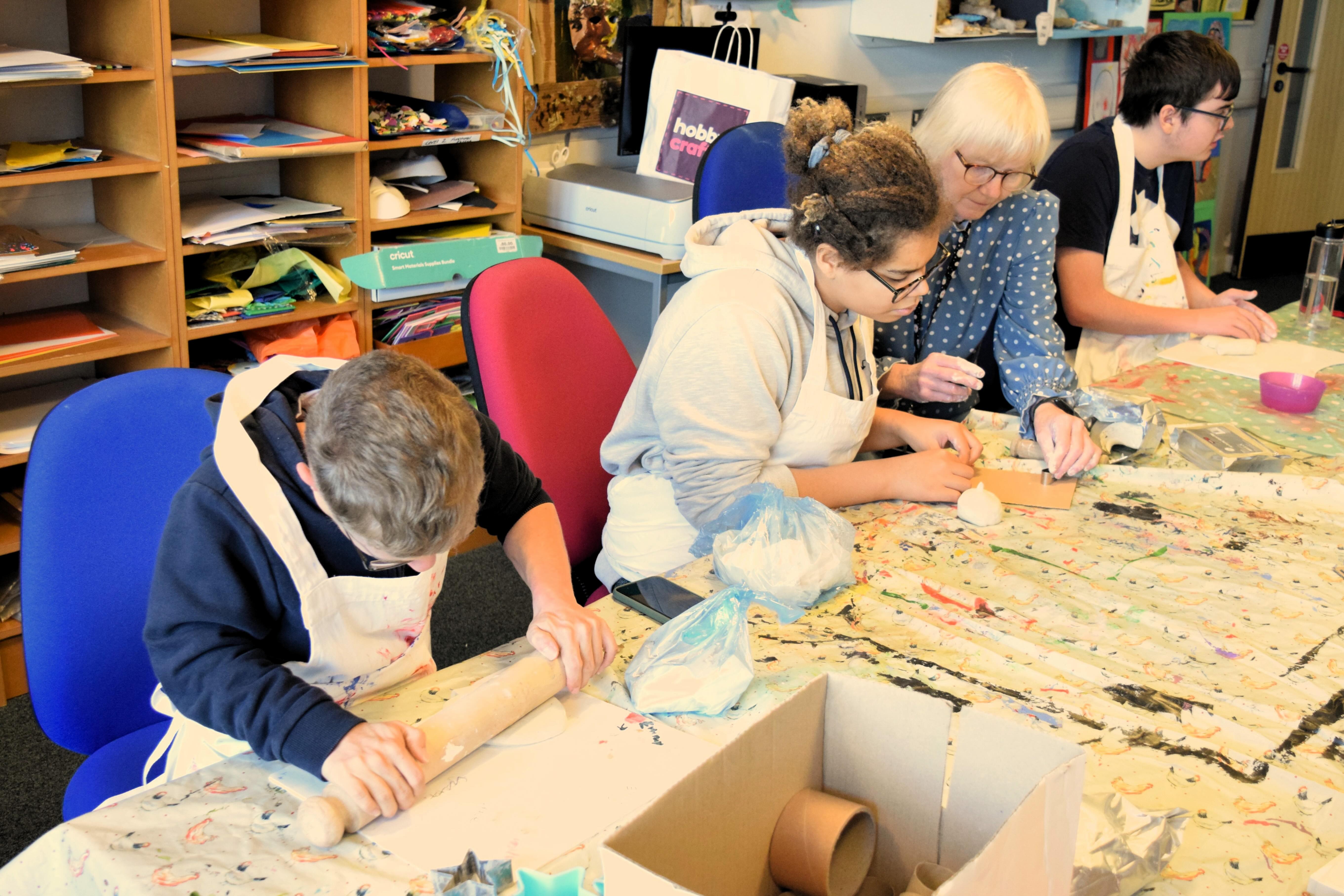 students in an art class rolling out clay - the teacher is helping one of the young people