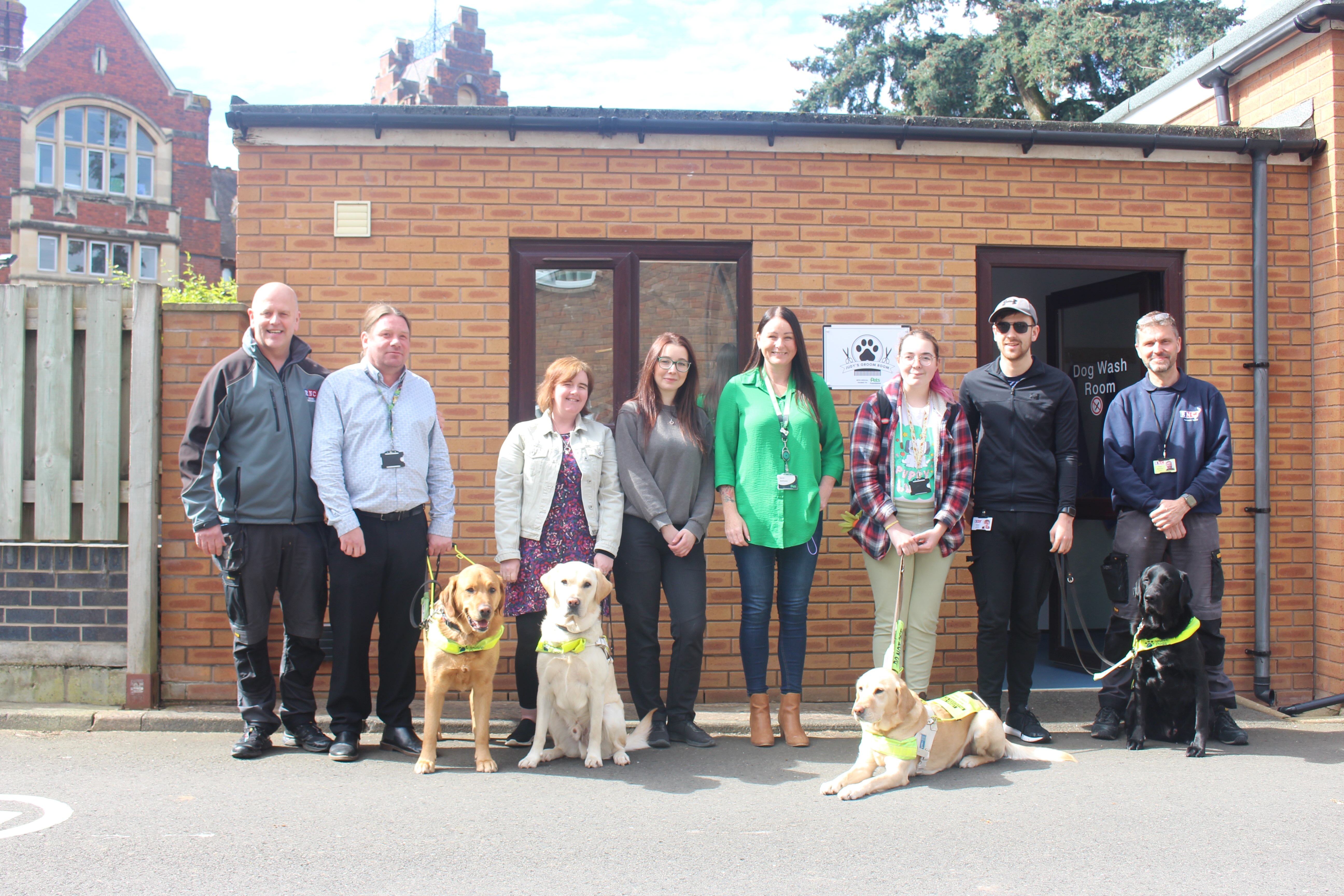 A group of staff and students standing outside the dog wash with four guide dogs