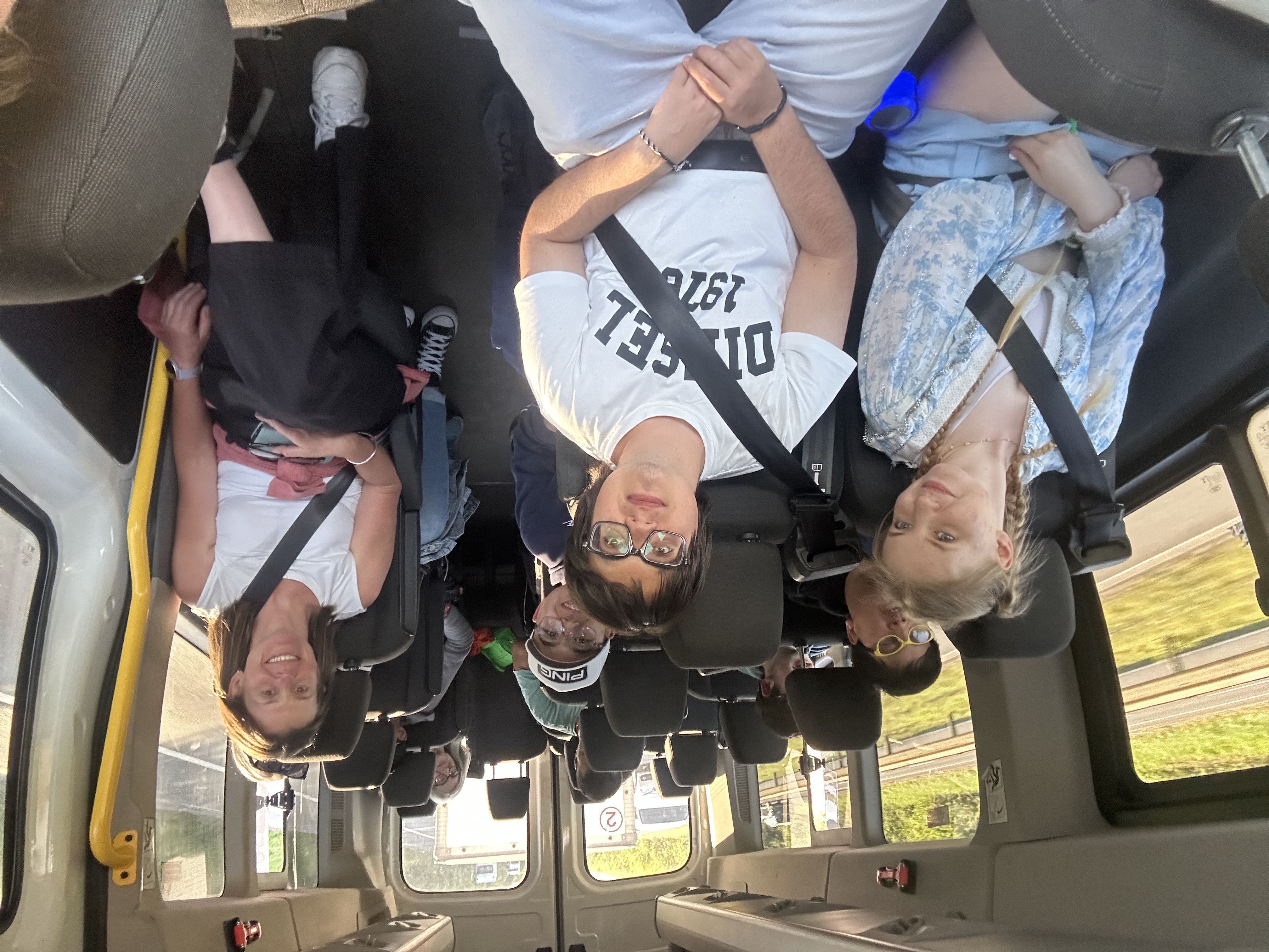 The group all sitting on the minibus wearing seatbelts and smiling