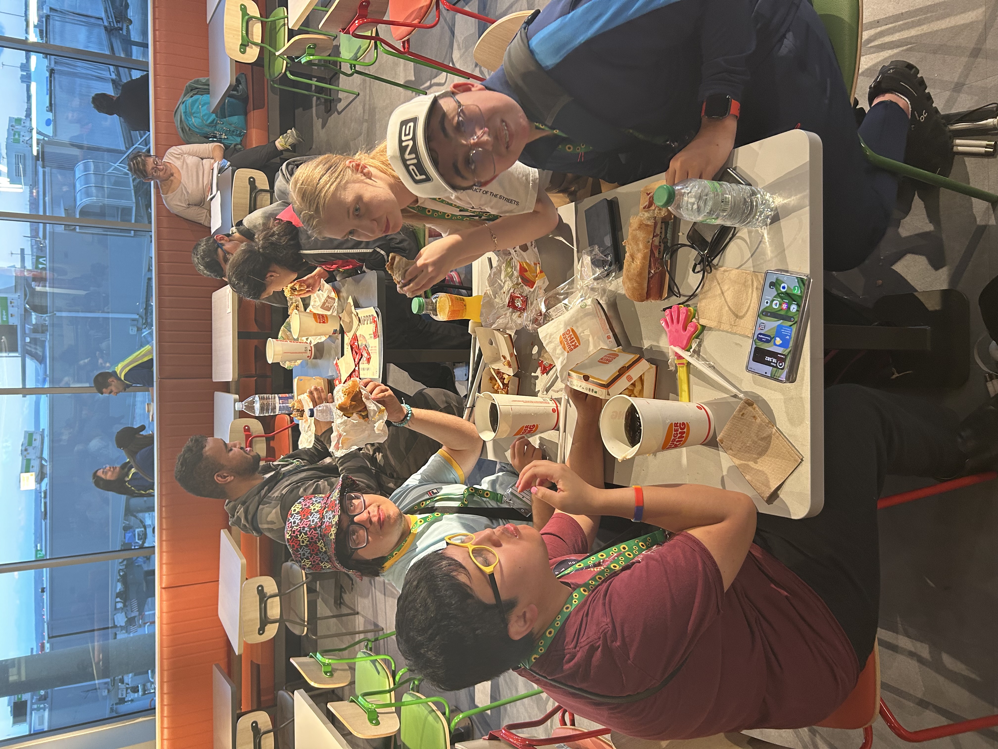 the group sitting round rectangular tables tucking into a meal at the airport