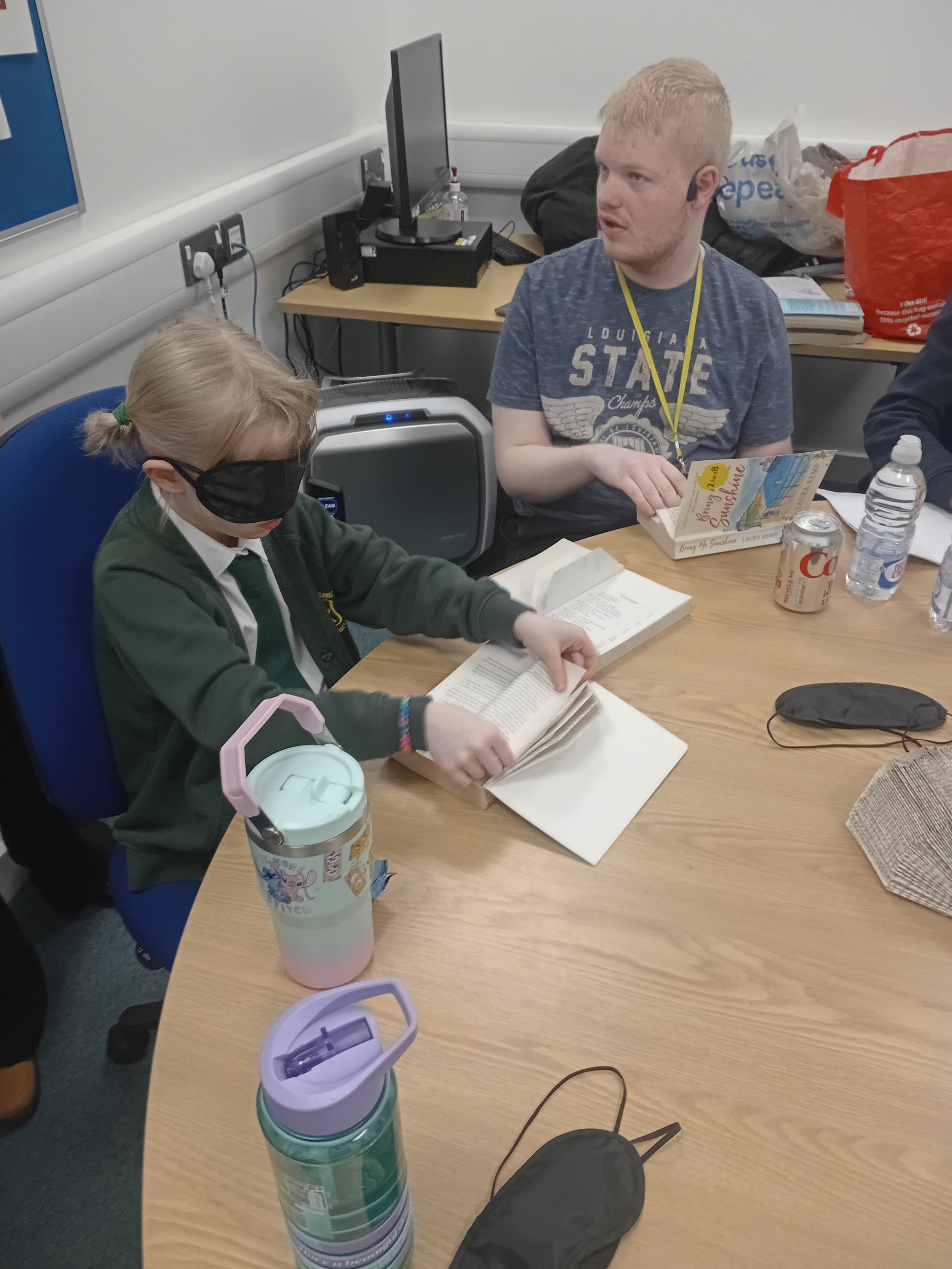 Logan assisting a blindfolded school pupil in making a book hedgehog