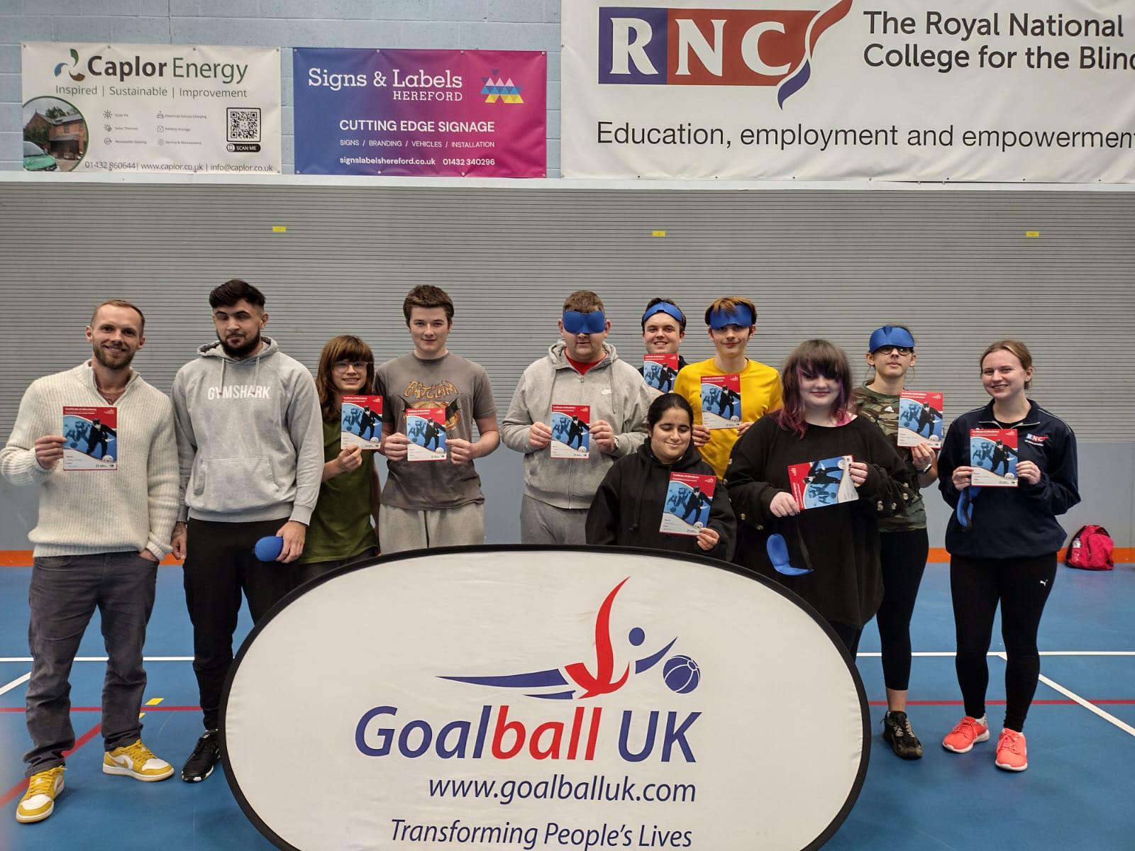 young people and staff line up in front a goalball banner displaying their certificates