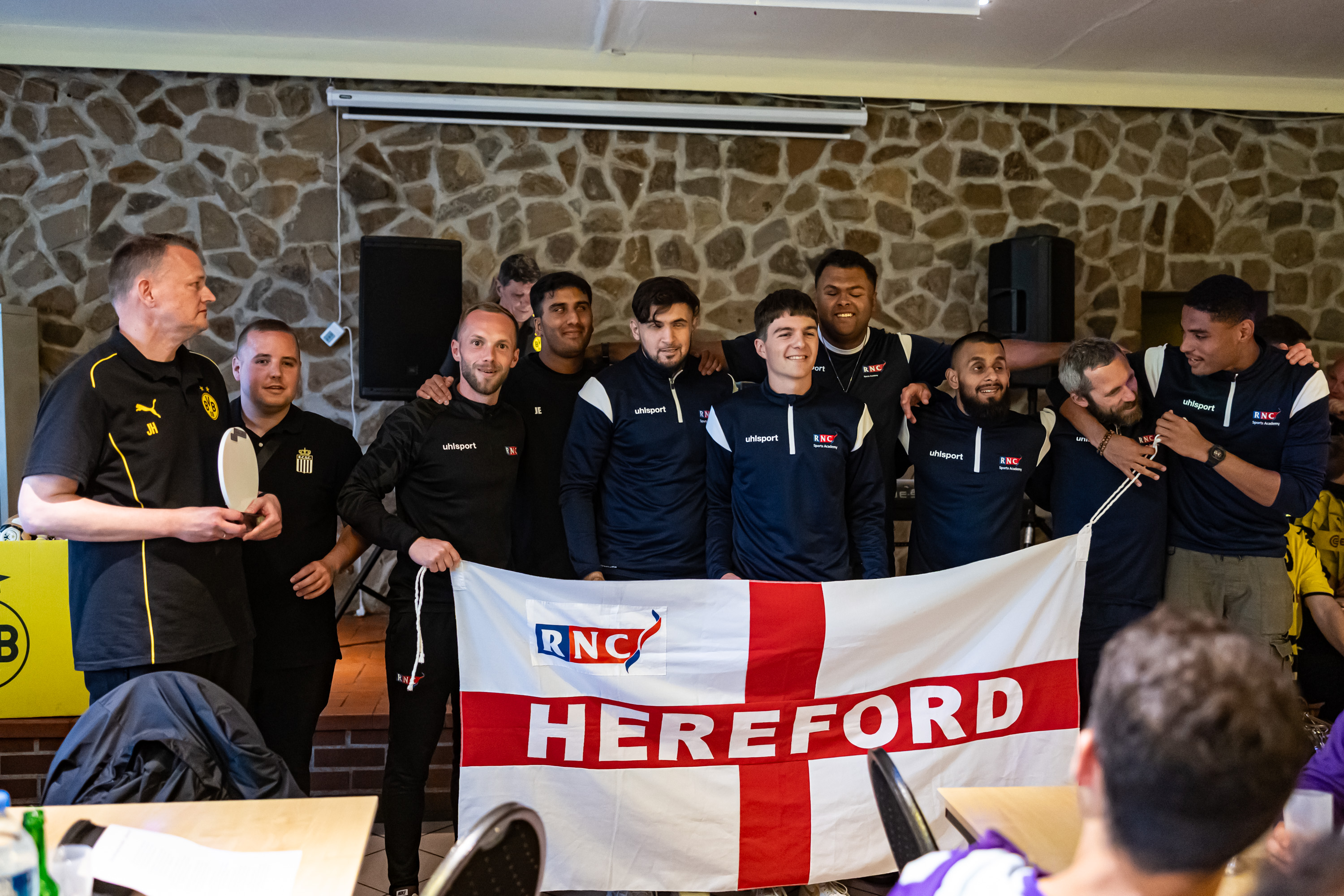 The team in their navy RNC tracksuits holding the RNC flag after being awarded the EBFL trophy